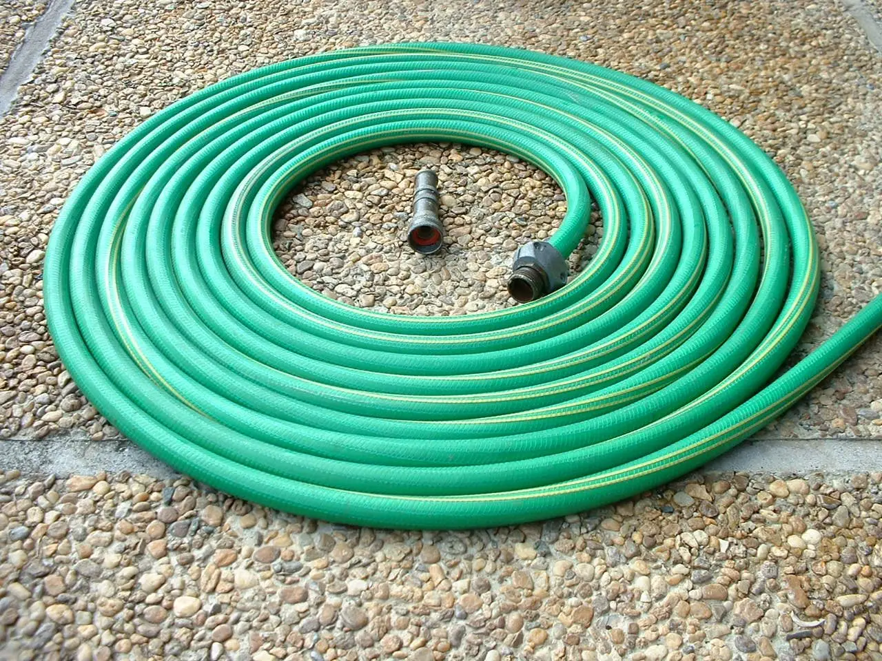 A green garden hose coiled on a patio with its fittings visible