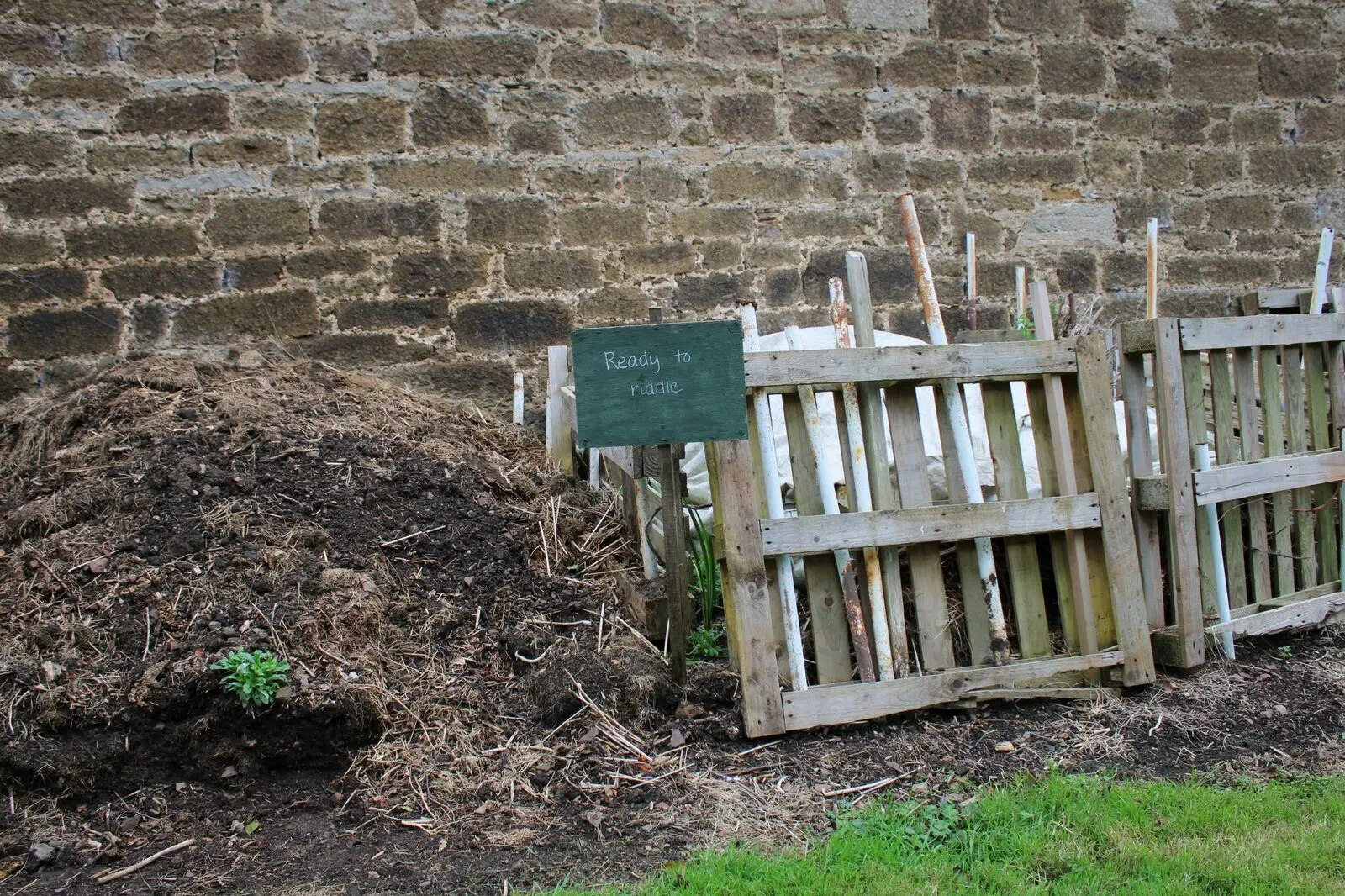 Open wooden compost bays holding a well-rotted heap against a stone wall