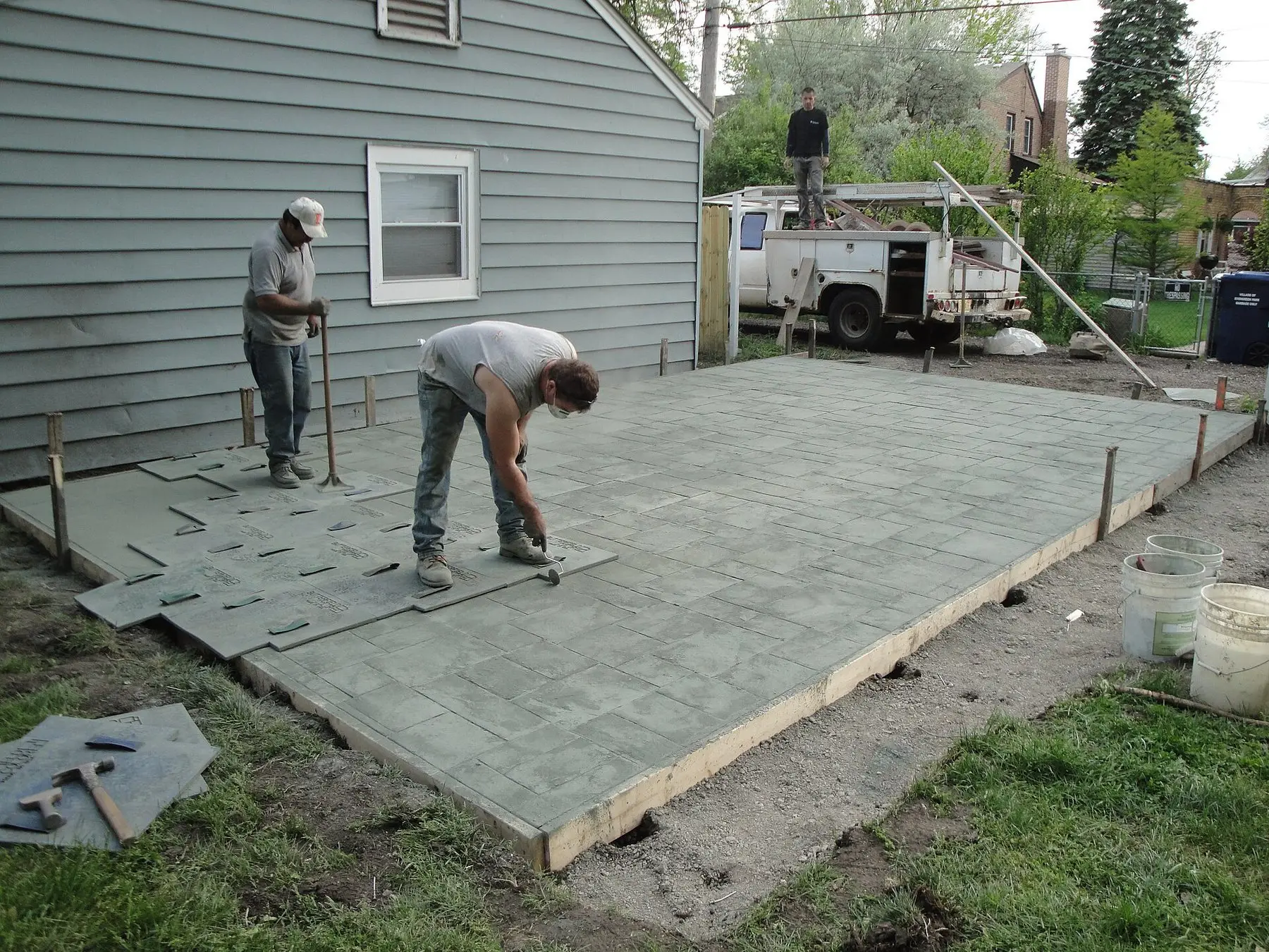 Two people working the surface of a freshly poured concrete slab inside its formwork