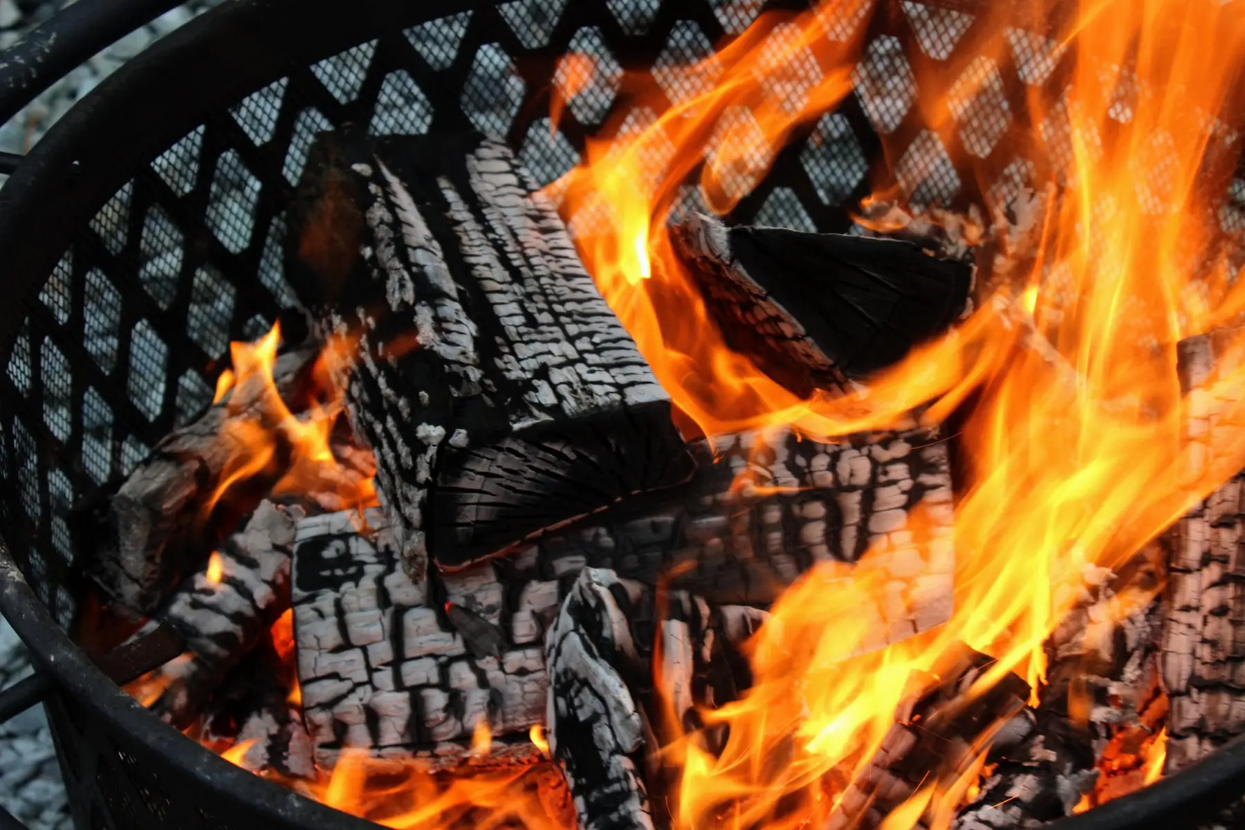 Logs burning inside a steel fire pit ring with a spark screen