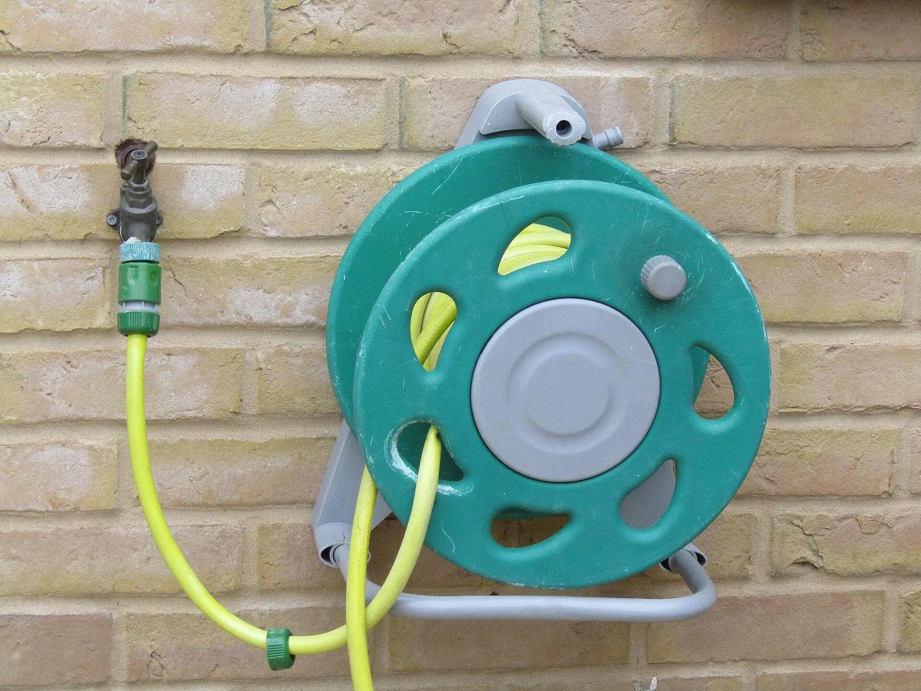 A wall-mounted hose reel fixed to a brick wall beside a tap
