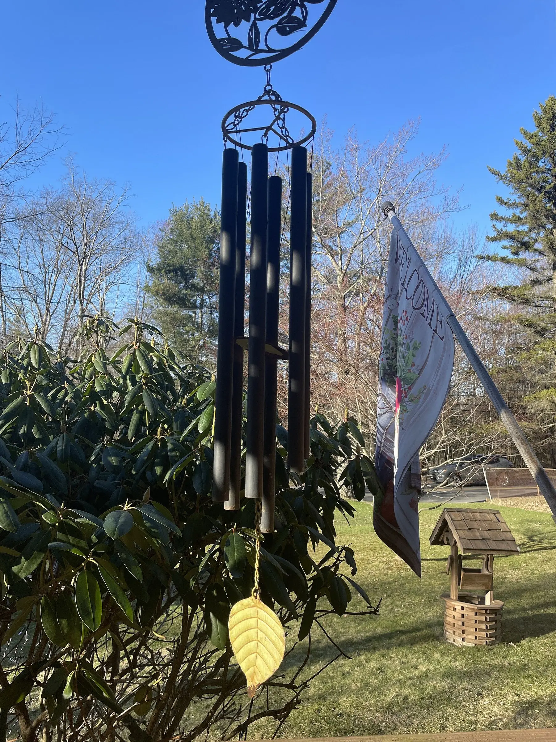 A metal tube wind chime with a leaf-shaped clapper hanging in a garden