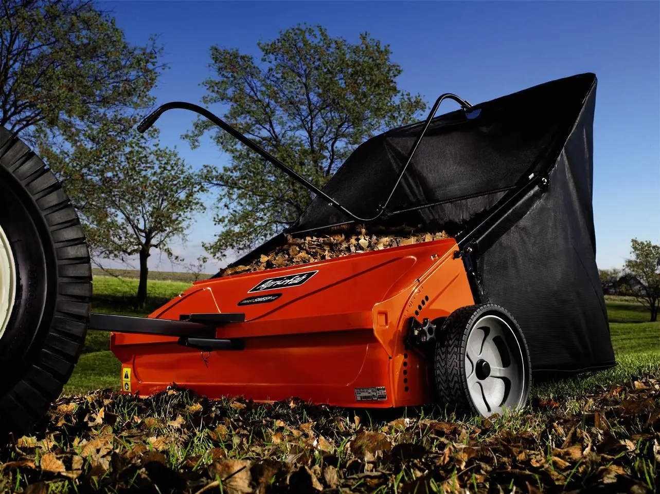 A push lawn sweeper with its hopper raised, standing on fallen leaves