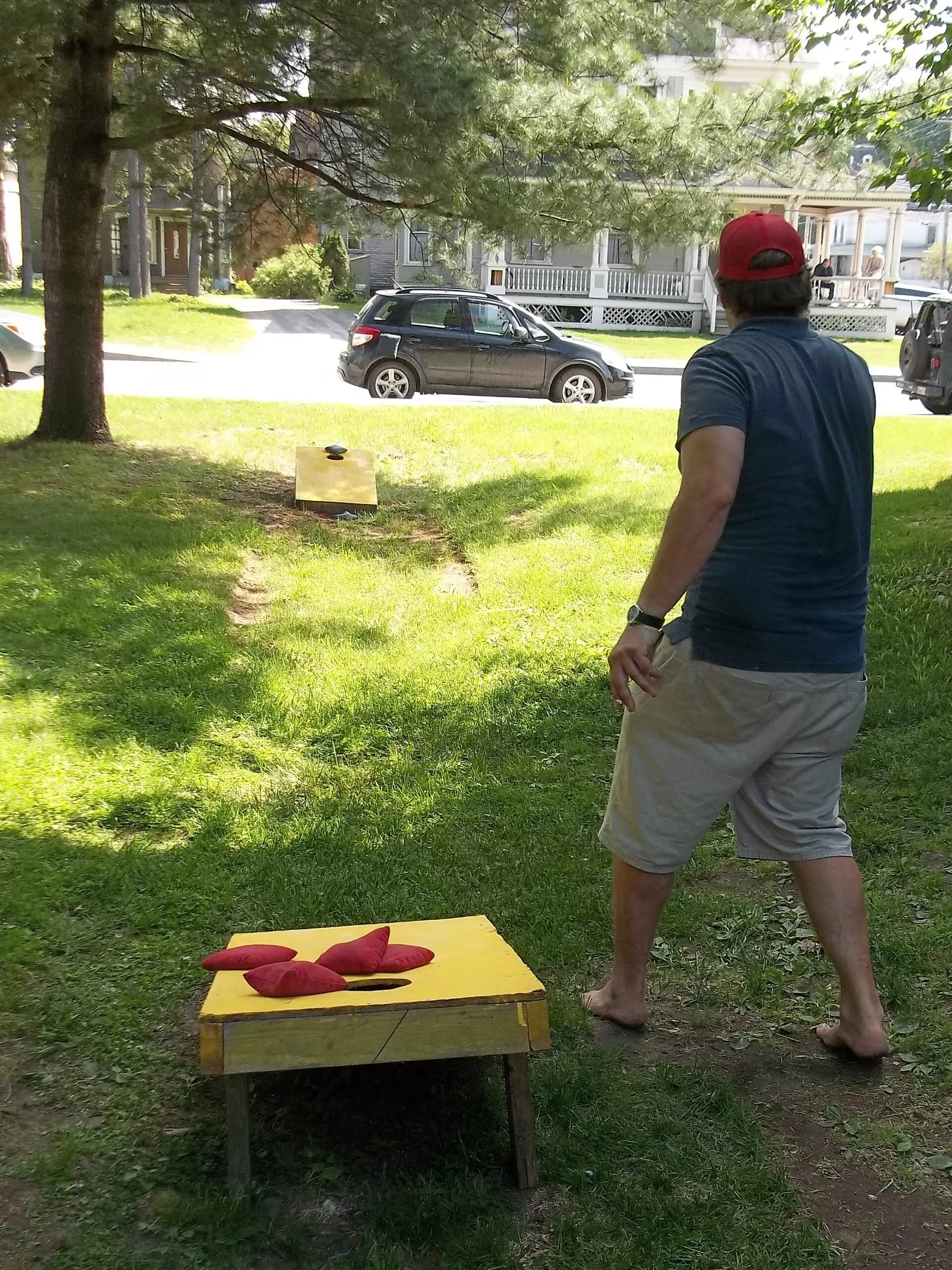 Someone throwing a bean bag at a cornhole board on a lawn